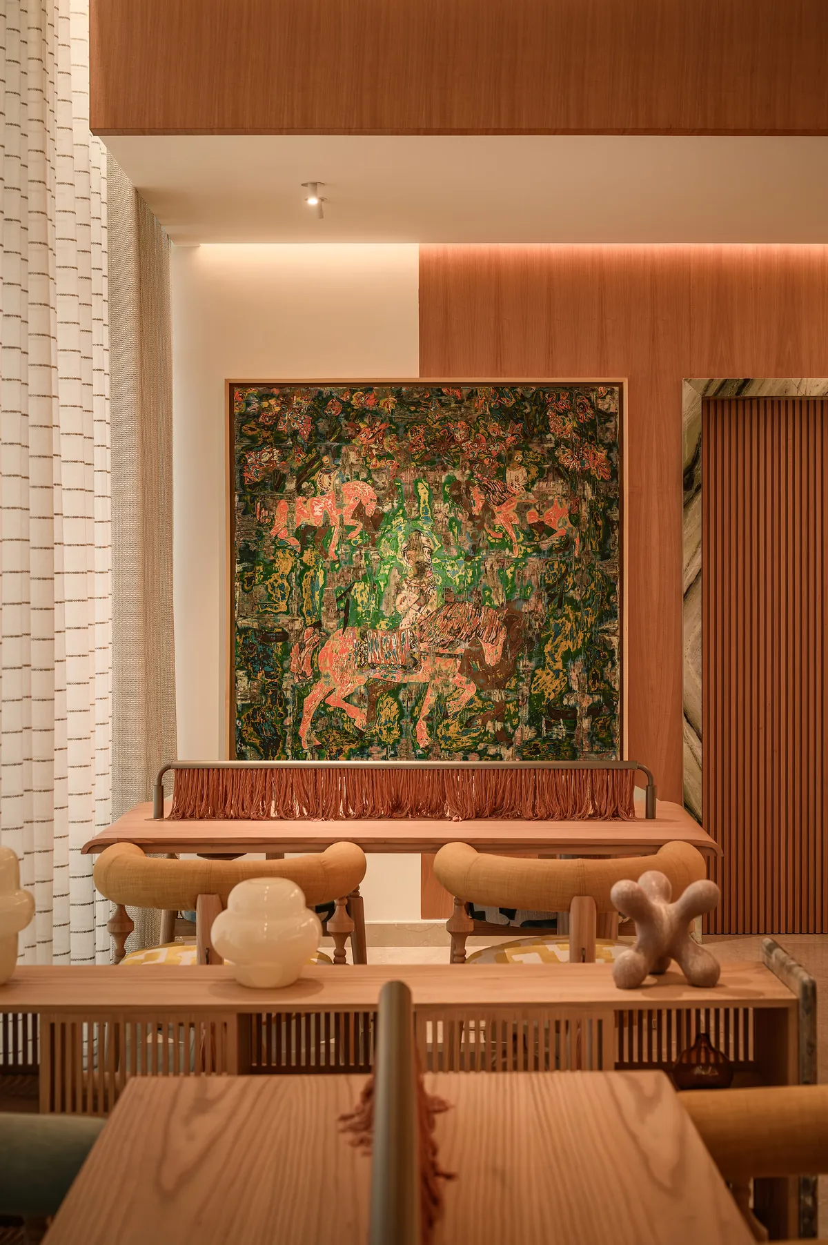 A large, richly coloured painting of horses and riders above a fringed oak console.