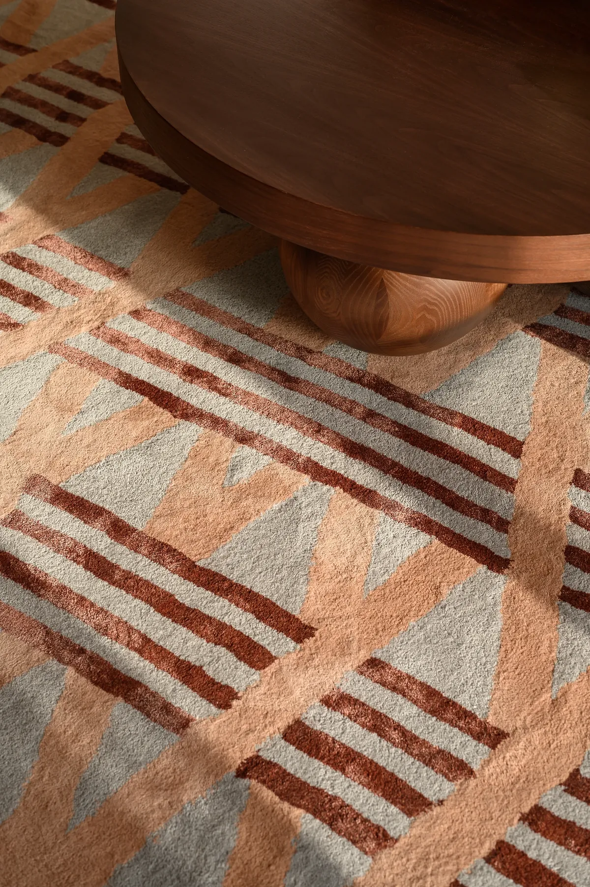 Detail of a hand-tufted rug in coral, clay and stone stripes beneath a walnut side table.