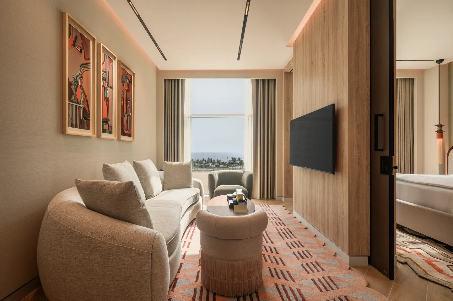 Junior Suite living room with a curved sofa, three framed artworks and a window onto the sea.