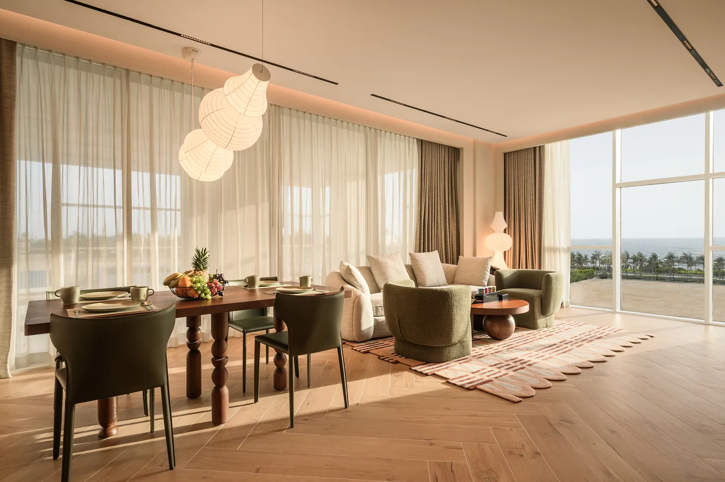 King Suite: a sunlit living and dining room with paper lanterns, olive armchairs and panoramic sea views.