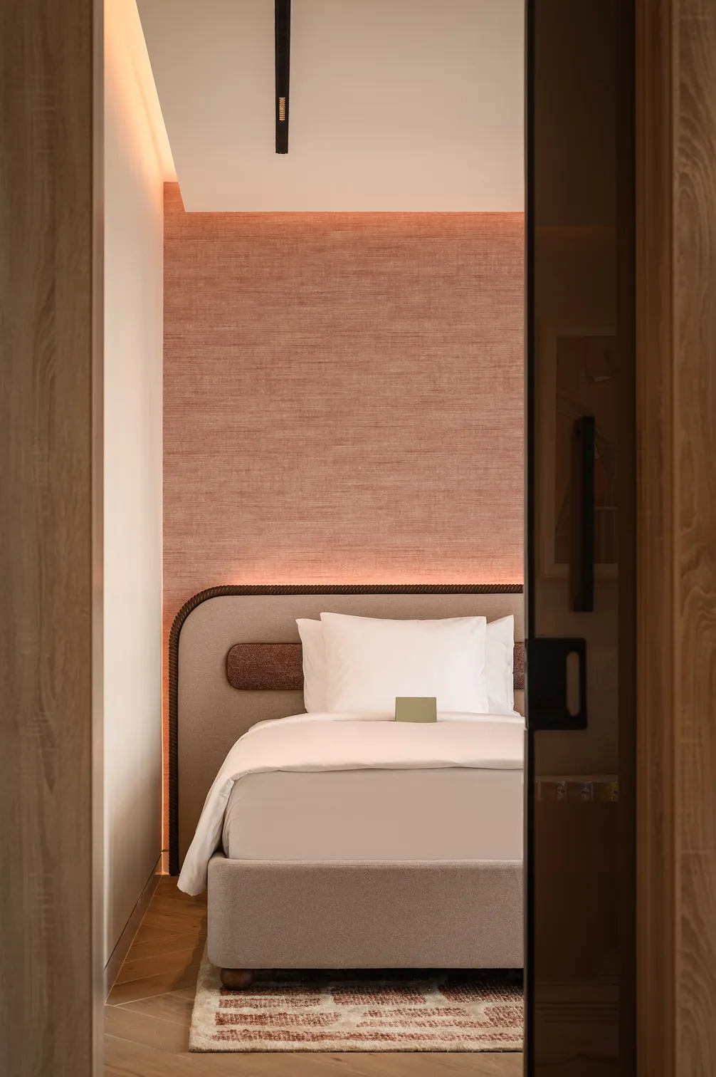 Superior Suite: a bed framed by a rope-trimmed headboard against a glowing coral linen wall.